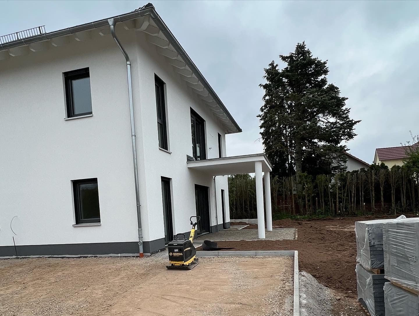 Verputztes Einfamilienhaus mit überdachter Terrasse, davor noch unbefestigte Baustellenfläche