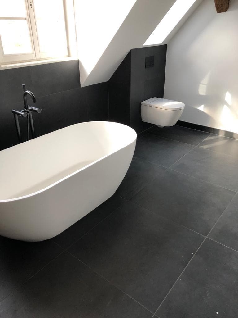 Designbad mit schwarzen Fliesen und freistehender weißer Badewanne